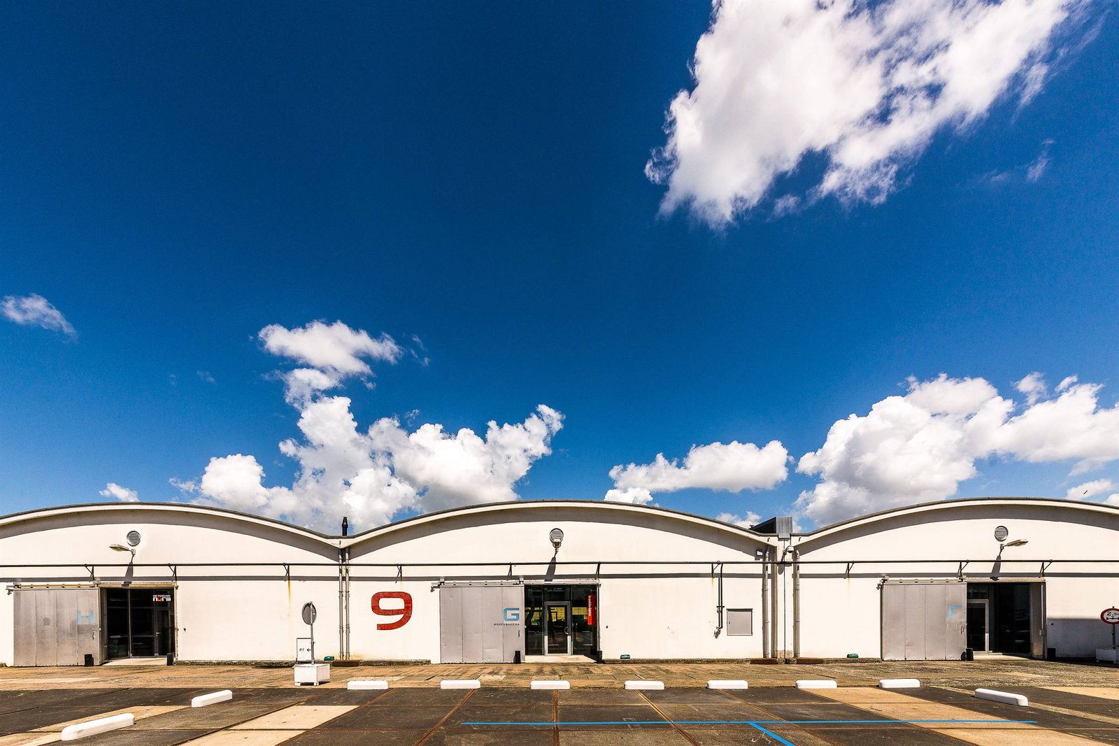 Zwei Hallen mit Tonnendächern und großer Freifläche unter blauem Himmel